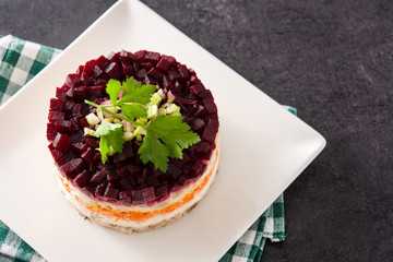 Traditional Russian herring salad with beetroot and carrots on black background. Copy space