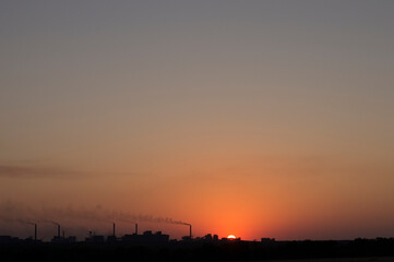 Fototapeta na wymiar the setting sun on the background of smoking chimneys industry