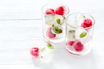 Cocktail glasses with berries in ice cubes on white table copy space