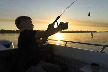 A boy on a fishing trip caught a fish.Fishing on the lake from a boat. Fishing rods in sunlight....