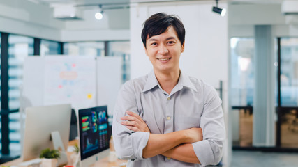 Portrait of successful handsome executive businessman smart casual wear looking at camera and smiling, arms crossed in modern office workplace. Young Asia guy standing in contemporary meeting room.