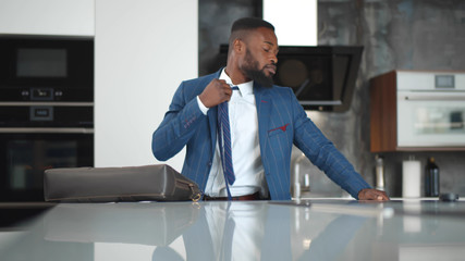 Tired afro-american businessman coming home after long workday, loosening tie in kitchen