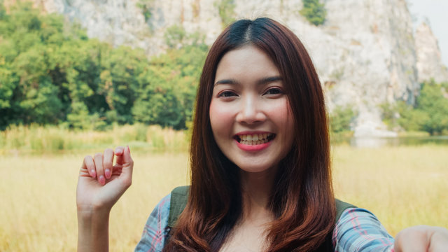 Cheerful young traveler Asian lady with backpack recording video vlog live streaming on phone upload in social media at mountain lake. Korean girl happy enjoy holiday trip. Lifestyle travel and relax.
