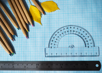  Wooden pencils metal ruler transparent plastic protractor and yellow autumn leaves on blue graph...