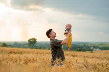 A young father holds his three month old son in his arms. Filmed in a wheat field.
