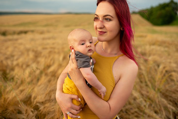 A mother tenderly holds her three month old son in her arms in a wheat field.