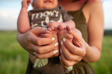 A mother holds the legs of her little three month old baby boy. Close-up.