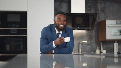 African smiling businessman enjoying morning coffee at his kitchen.