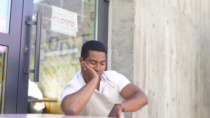 Black waiter of street cafe is waiting for clients, customers he is bored, no people in their food restaurant, everyone in self-isolation, quarantine.