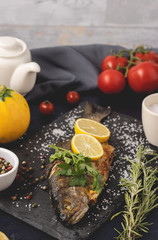 Grilled trout with olive oil, parsley, pepper, salt and lemon placed on the dark background. Healthy Mediterranean food and dieting concept. Served and ready to eat.