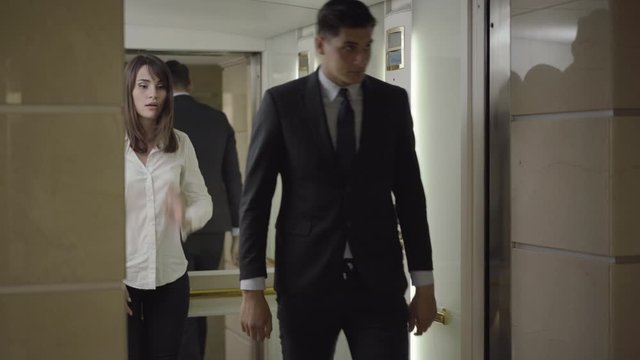 Young Caucasian man and woman hugging and kissing on business center. Elevator door opens and embarrassed couple walking out. Portrait of passionate colleagues flirting in office.