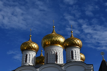 Golden domes with a cross on the background of blue sky and clouds.