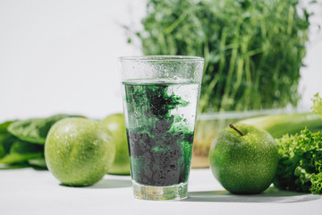 chlorophyll in a glass of water on a white background near are various fresh vegetables fruits and...