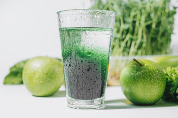 chlorophyll in a glass of water on a white background near are various fresh vegetables fruits and...