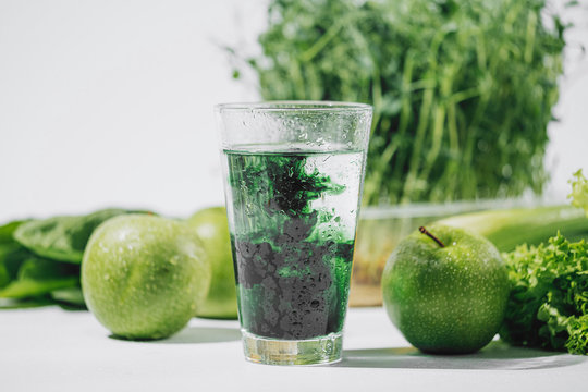 chlorophyll in a glass of water on a white background near are various fresh vegetables fruits and roots with lettuce and spinach