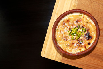 Traditional Arabic, eastern dessert Om Ali. Top view. Egyptian Bread Pudding in a brown bowl on light oak tray on dark wooden table with copy space. Top view. Egypt sweet pastry dessert