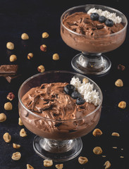 Tasty chocolate mousse dessert placed on dark background with hazelnuts, dark chocolate, blueberries and whipped cream decoration. Close up view.