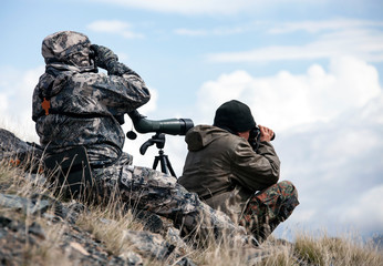 Hunting  in the  mountains determine trophy quality animals through binoculars and a telescope.