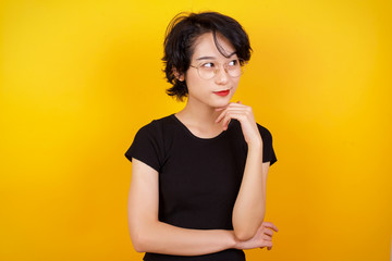 Obraz premium Dreamy female with pleasant expression, wearing casual clothes, looks sideways, keeps hand under chin, thinks about something pleasant, poses against gray background.