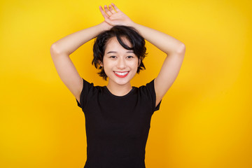 Portrait of beautiful brunette female looks with excitement at camera, keeps hands raised over head notices something unexpected, isolated over gray wall. Lovely woman reacts on sudden news.