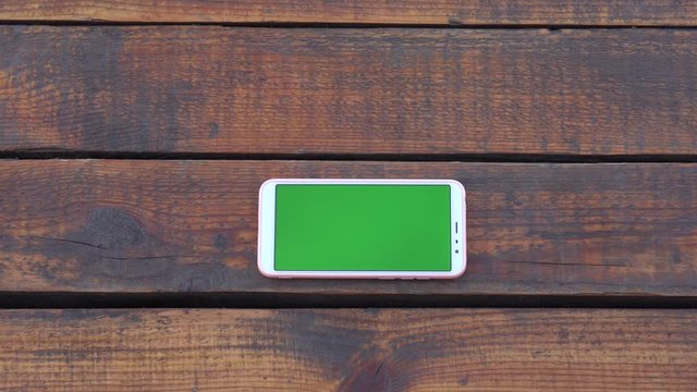 Wooden workplace. Smartphone with empty green blank screen isolated on brown weathered wood vintage table or floor background. Copy space for your own video or text, top view flat lay 4k footage.