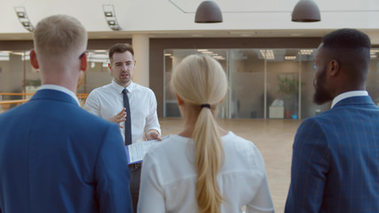 Back view of business team standing in office lobby listening to young man coach