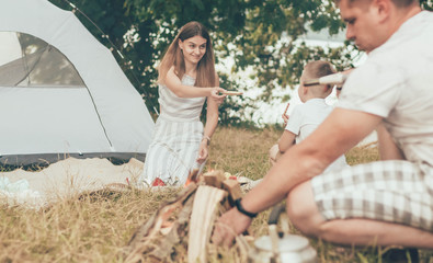 Obraz na płótnie Canvas Family resting in nature with a tent mom stretches out her hand to give the child cookies on the background father lights a fire