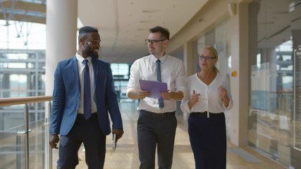 Fototapeta premium Interracial business colleagues walking along corridor and discussing project