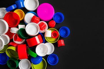 Top view of a pile of plastic bottle caps on a black background with copy space. Recycled plastic bottle caps. Separate garbage collection. Recycling of plastic for prosthetics. Selective focus.
