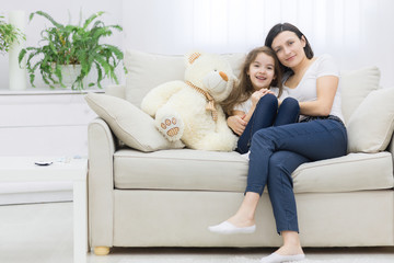 Photo of mother and her daughter sitting together on white sofa.