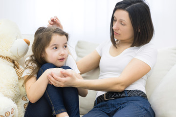 Close up photo of sad little girl sitting on the sofa and her mom hugging her.