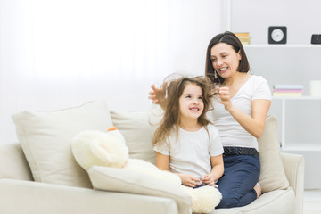 Obraz premium Photo of young mother making hair for her little daughter.