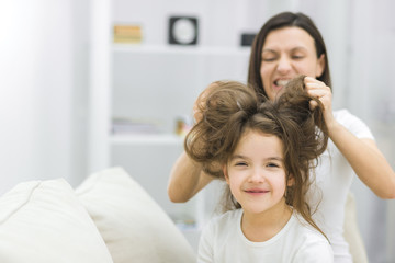 Photo of small girl with long dark messy hair and her mother brushing her hair.