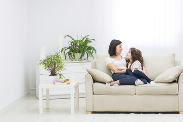 Photo of beautiful mother hugging with her cute little daughter and look each other in living room.