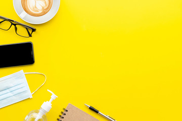 New preventive mask, eyeglasses, smartphone, hand sanitizer gel, coffee cup and book on yellow background with copy space for text or design. Coronavirus disease (COVID-19) or Healthy concept