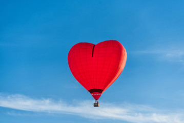 Fototapeta na wymiar Red heart-shaped air balloon flies against the blue sky. Postcard concept