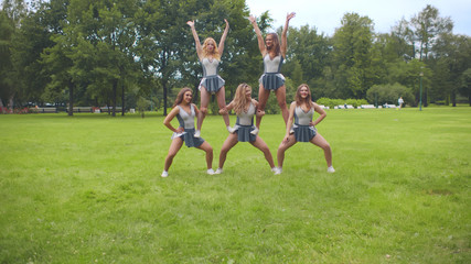 Young beautiful cheerleaders performing pyramid working out in summer park