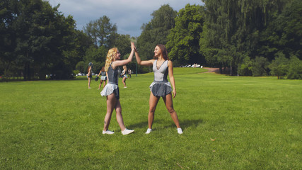 Cheerleader girlfriends giving each other high-five training outdoors