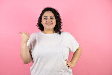 Young beautiful woman over isolated pink background pointing thumb up to the side smiling happy