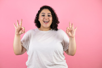 Pretty woman very happy doing the “okey” sign with both hands. Standing over isolated pink background