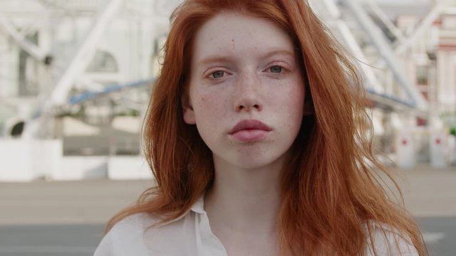 Attractive red-haired young woman with cute face freckles looking serious into camera outside the street city center. Beautiful ginger. Female portraits.