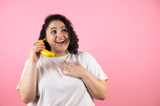 Young beautiful woman over isolated pink background smiling and using a banana as a phone