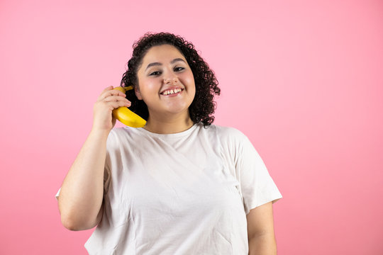 Young beautiful woman over isolated pink background smiling and using a banana as a phone
