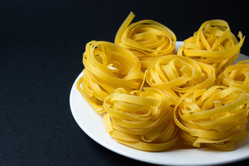 nests of pasta on a black background. Italian pasta. The pasta nests are on a white plate. European cuisine
