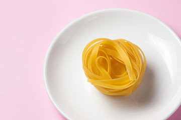 nest of pasta on a pink background. Italian pasta. One nest of pasta lies on a white plate. European cuisine