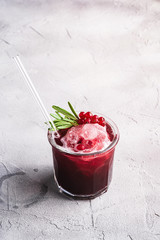 Fresh ice cold fruit cocktail in glass with reusable straw, refreshing summer red currant berry drink with rosemary leaf on stone concrete background, angle view