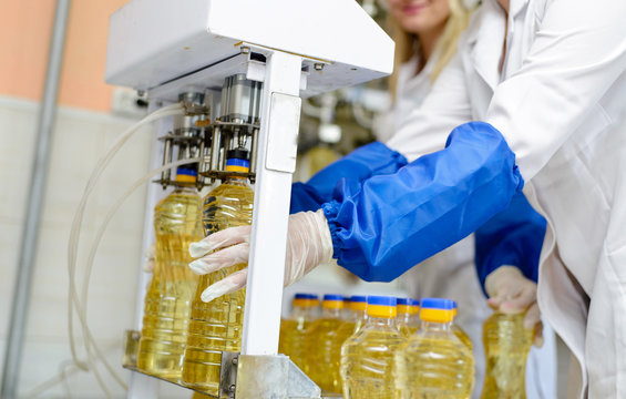 line of production of refined sunflower oil. Girl worker at a factory on a conveyor background with bottles of vegetable oil. - Powered by Adobe
