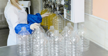 line of production of refined sunflower oil. Girl worker at a factory on a conveyor background with bottles of vegetable oil.
