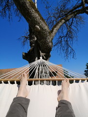 Faulenzen mit nackten Füßen auf einer Weißen Hängematte unter strahlend blauem Himmel im Sommer...