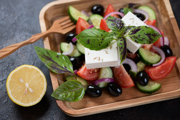 Close-up of greek salad made of sliced tomatoes, cucumbers, olives, feta cheese and fresh green basil, selective focus